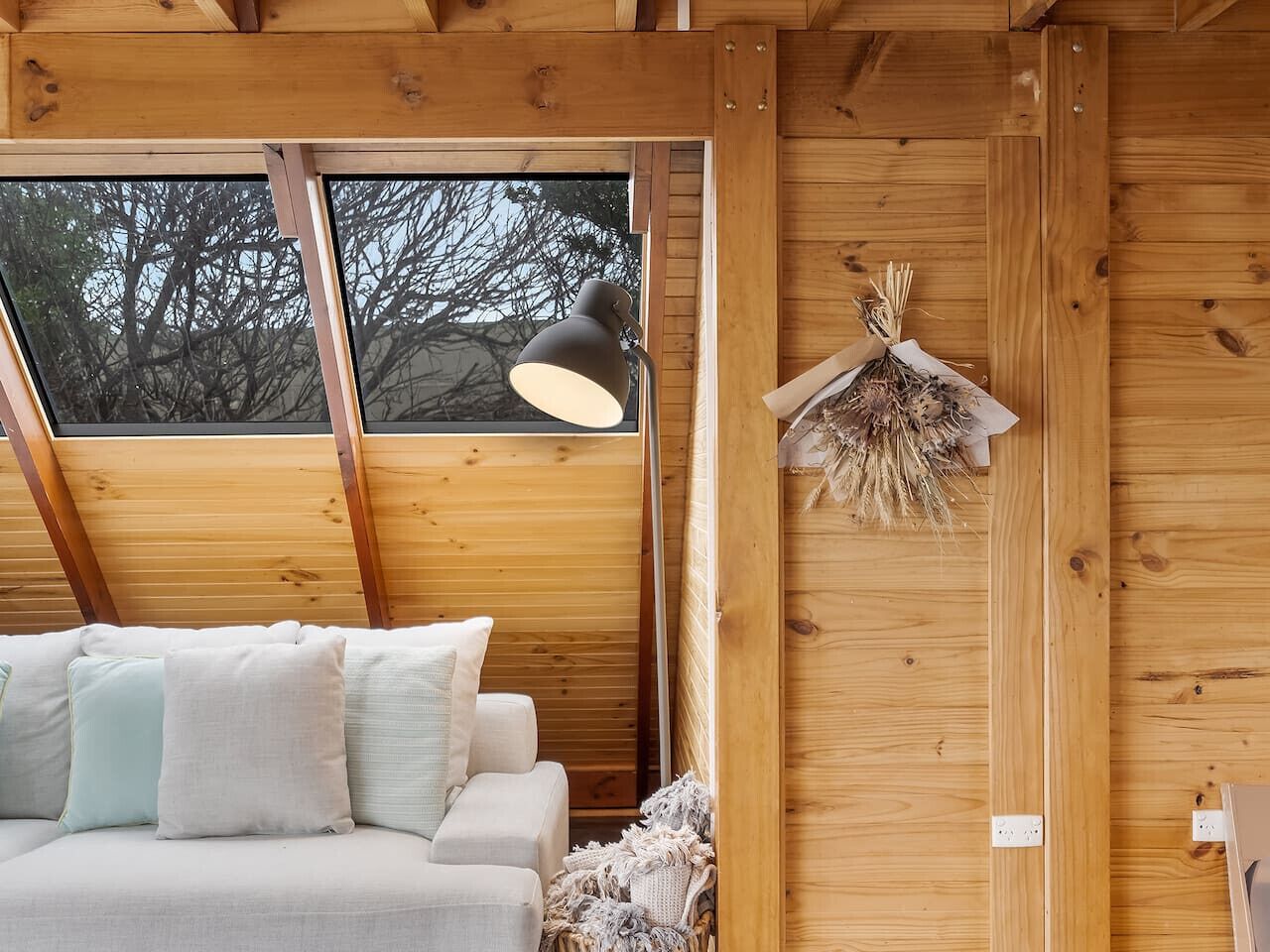 A cozy wooden cabin interior with a sofa, a lamp, and a decorative wreath on the wall.