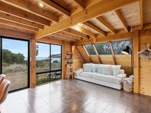 Ein geräumiges Zimmer mit einem weißen Sofa, Holzbalken, großen Fenstern und Blick ins Freie.
