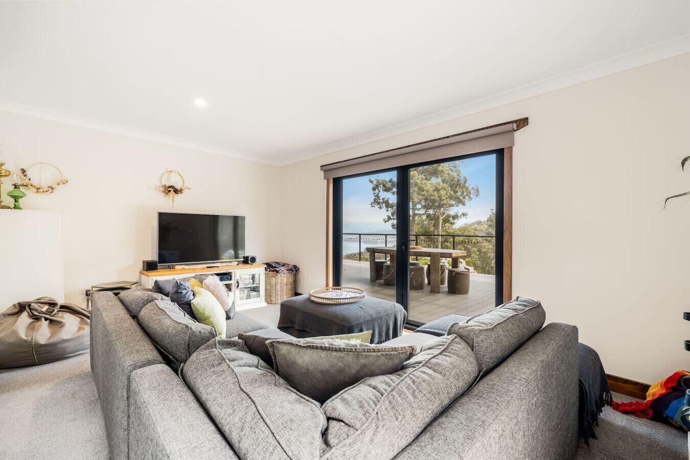 Ein modernes Wohnzimmer mit großem Flachbildfernseher, grauen Sofas und einem Balkon mit Meerblick.