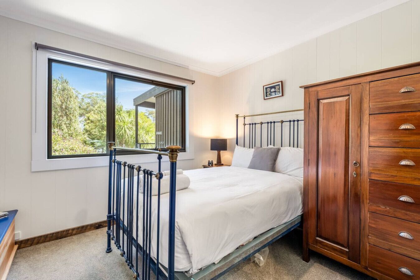 A bedroom with a bed, a nightstand, a wardrobe, and a window with a view of trees.