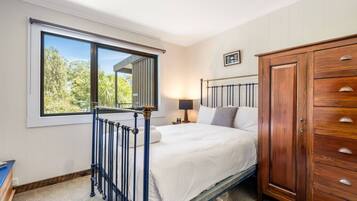 A bedroom with a bed, a nightstand, a wardrobe, and a window with a view of trees.