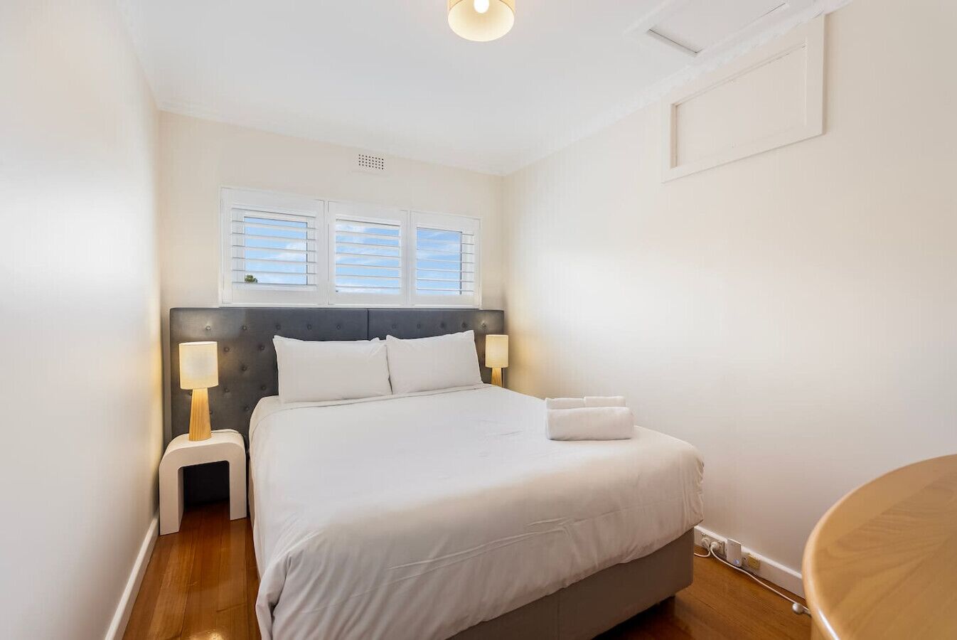 A neatly arranged bedroom with a large bed, two bedside lamps, and a window with blinds.