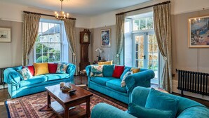 A room with two blue sofas, a wooden coffee table, a patterned rug, a clock, and a painting on the wall.
