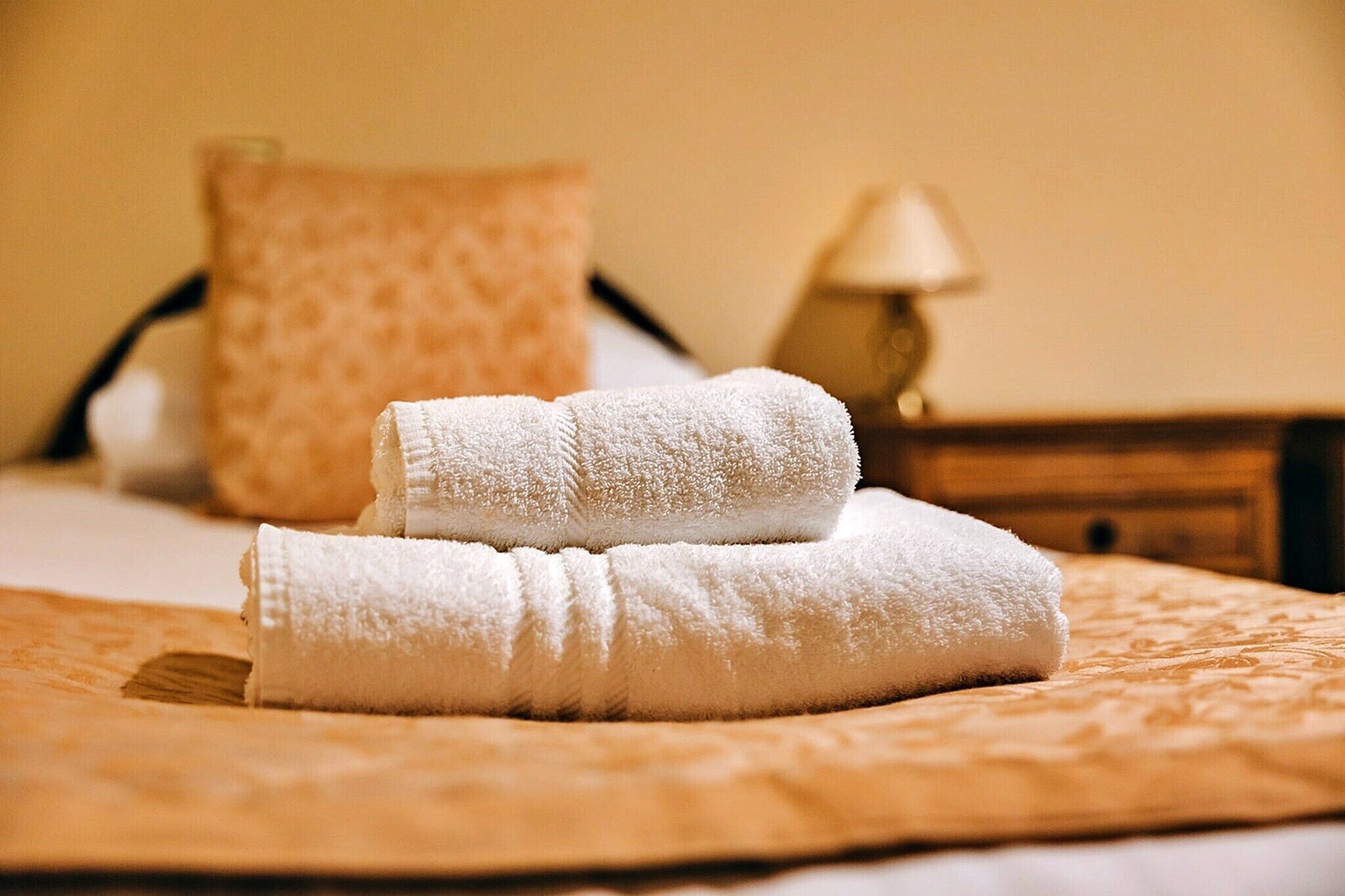 A neatly made bed with a folded white towel and a pillow.