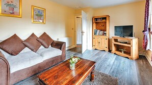 A living room with a brown sofa, a wooden coffee table, a bookshelf, and a television. - 2 bedroom cottage in Dorrington, No Deposit (Dorrington)