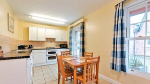 A compact kitchen with white cabinets, a dining table with chairs, a coffee maker, and a window with curtains. - Cottage in UK near Scenic Beaches & Trails (Dorrington)