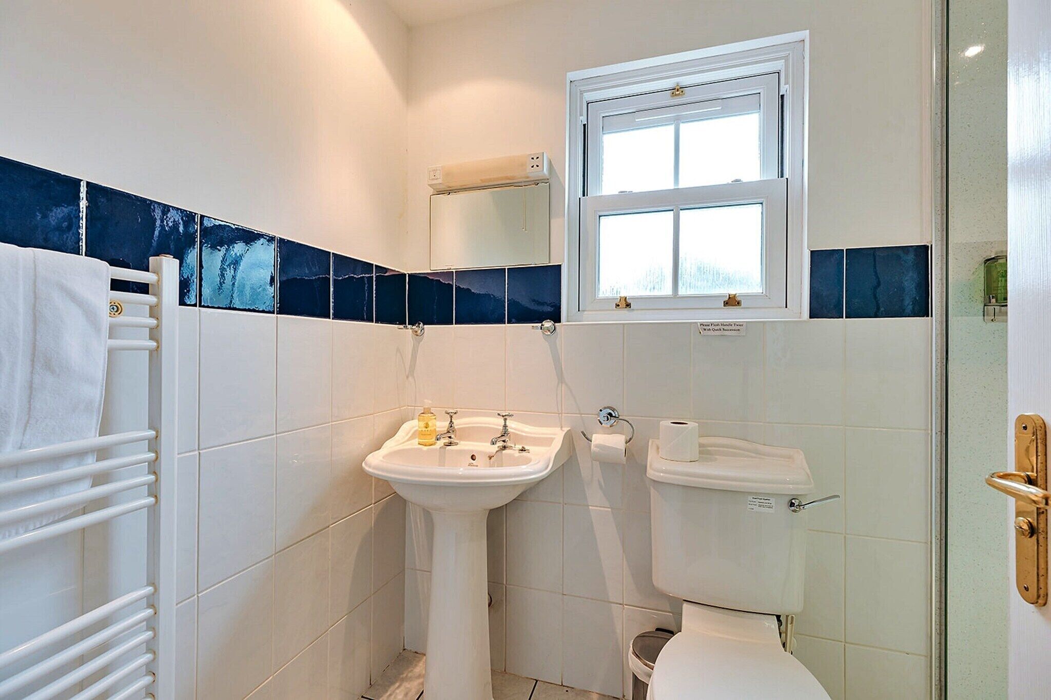 A bathroom with white tiles, a sink, a toilet, a towel rack, and a window.