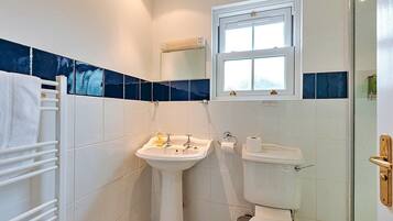 A bathroom with white tiles, a sink, a toilet, a towel rack, and a window.
