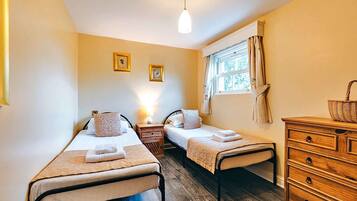 A room with two single beds, a wooden dresser, a window with curtains, and a hanging light fixture.