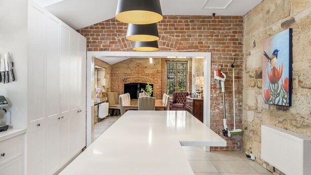 A kitchen with a central island, white cabinets, a brick wall, and a hanging light fixture. - Bellevue House Historic Luxury (Richmond)