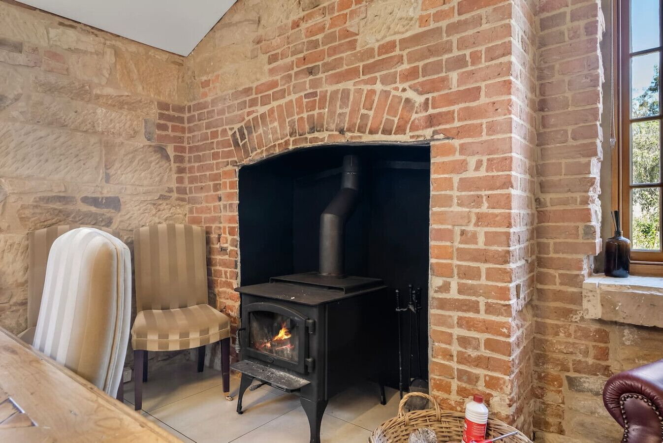 A room with a brick fireplace, a chair, and a table with a bottle.