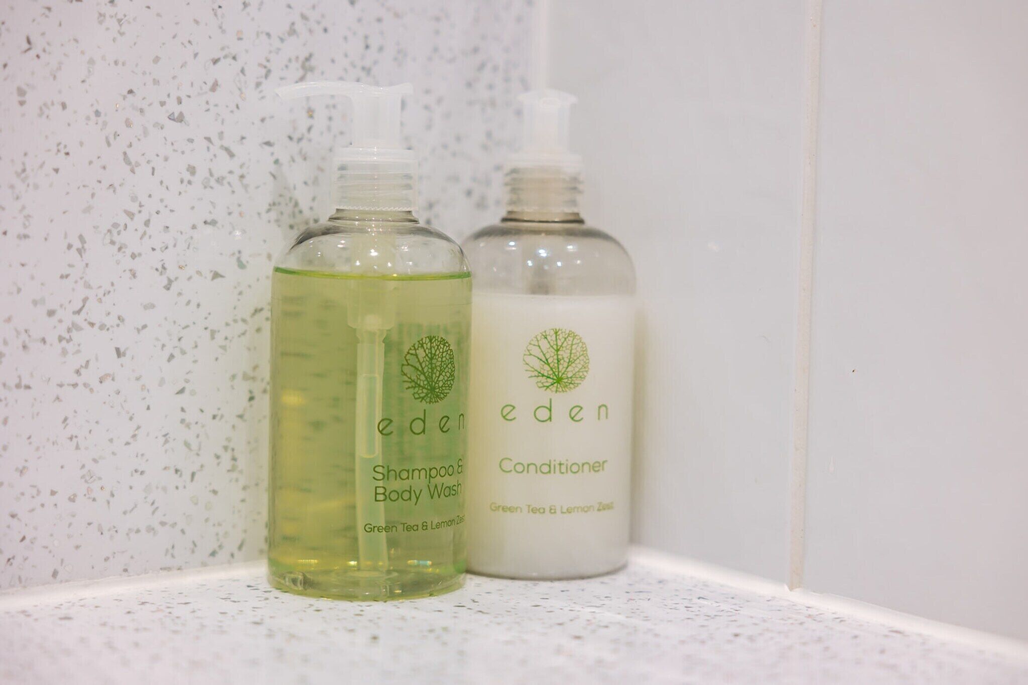 Deux bouteilles de shampoing et d’après-shampoing de la marque Eden, posées sur une étagère blanche.