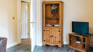 A room with a wooden cabinet, a television on a wooden stand, and a door leading to another room. - Cottage in Netley Hall with Lush Gardens (Dorrington)