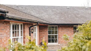 A brick building with two windows and a door, a chimney, and a small garden area with plants. - Cottage in Netley Hall with Lush Gardens (Dorrington)