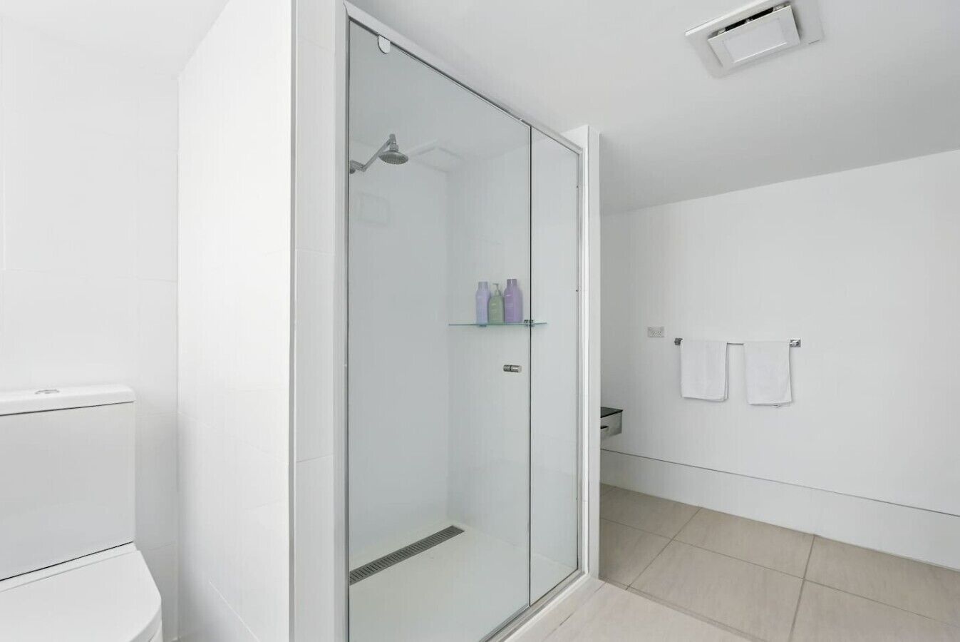 Une salle de bain moderne avec une douche à parois de verre, des carreaux blancs et des toilettes.