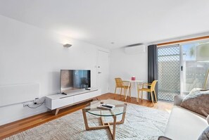 Uma sala de estar moderna com televisão de tela plana, mesa de centro de vidro, um sofá e uma área de jantar com cadeiras.