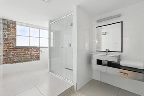 A modern bathroom with a glass shower enclosure, a white sink with a mirror, and a brick wall.