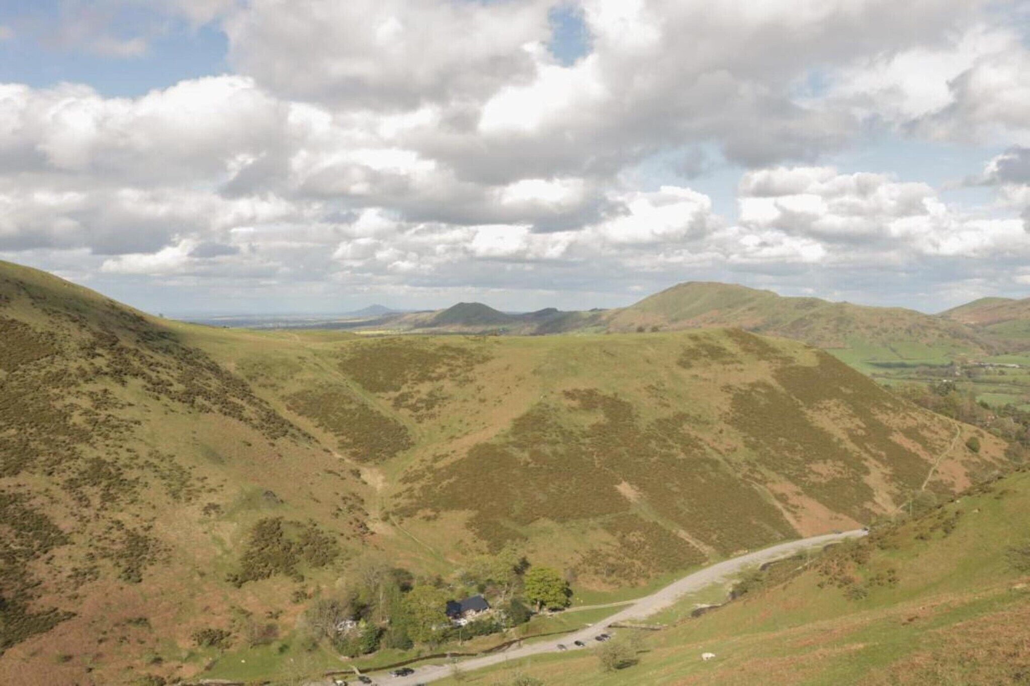 A rural landscape with rolling hills, a winding road, and a small building with a green roof.