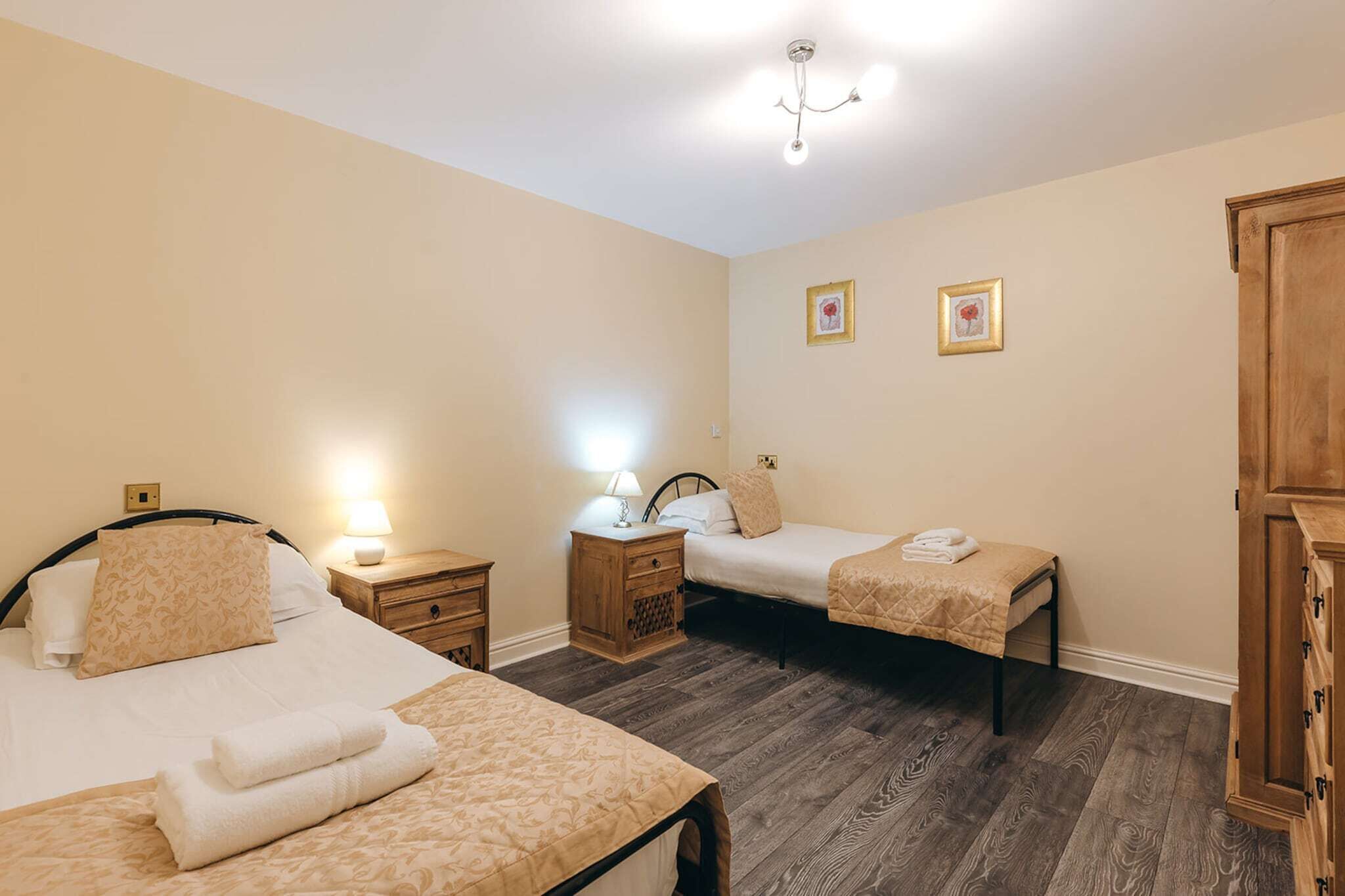 A hotel room with two beds, wooden flooring, a wardrobe, and a chandelier.