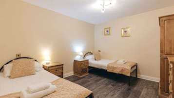 A hotel room with two beds, wooden flooring, a wardrobe, and a chandelier.