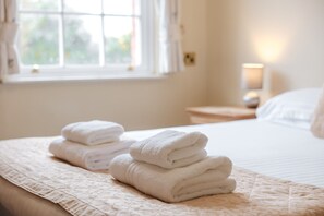 A neatly made bed with folded white towels and a window with curtains. - Cottage in Dorrington near Netley Hall (Dorrington)