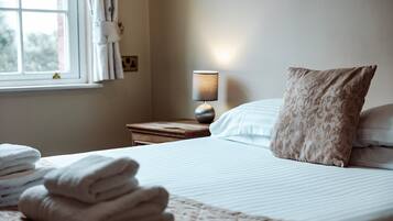 Een net opgemaakt bed met een kussen, een bedlamp en een raam met gordijnen.