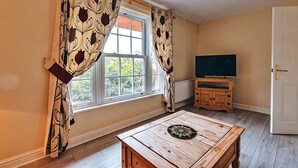 A room with a wooden table, a television on a cabinet, and a window with curtains.