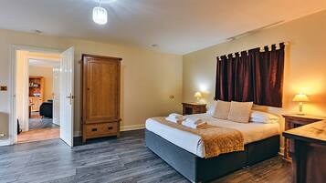 Un dormitorio con una cama grande, un armario de madera, dos mesitas de noche con lámparas, y una puerta que da al baño.