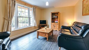 A living room with a leather sofa, wooden coffee table, and a television. - Cottage in Netley Hall with Scenic Trails (Dorrington)