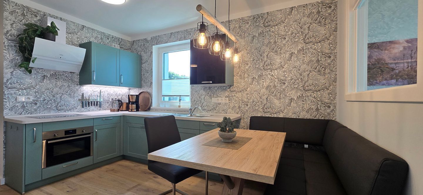A modern kitchen with teal cabinets, a wooden dining table, and a black sofa.