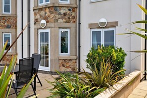 A corner of a building with stone and plaster exterior, a window with a white frame, and a planter with green plants. - Apartment in Carbis Bay with Stunning Sea Views (St Ives)