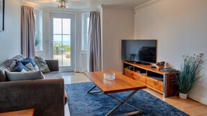 A modern living room with a sofa, a coffee table, a TV, and a wooden entertainment unit. - Apartment in Carbis Bay with Stunning Sea Views (St Ives)