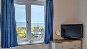 A room with a window, curtains, a television, a small table, and a radiator. - Apartment in Carbis Bay with Stunning Sea Views (St Ives)
