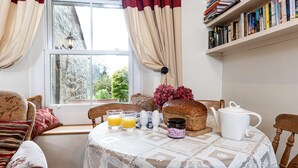 A cozy breakfast setup with a table, chairs, a bookshelf, and a window with curtains. - Cottage in Settle near Yorkshire Dales (Settle)