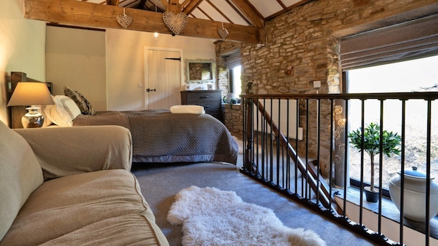 A bedroom with a bed, a sofa, a stone wall, a wooden ceiling, and a balcony with a railing. - Barn in Peak District near Buxton (Buxton)