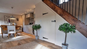 A modern kitchen with white cabinets, a dining area with a wooden table and chairs, and a staircase with a wooden railing. - Barn in Peak District near Buxton (Buxton)