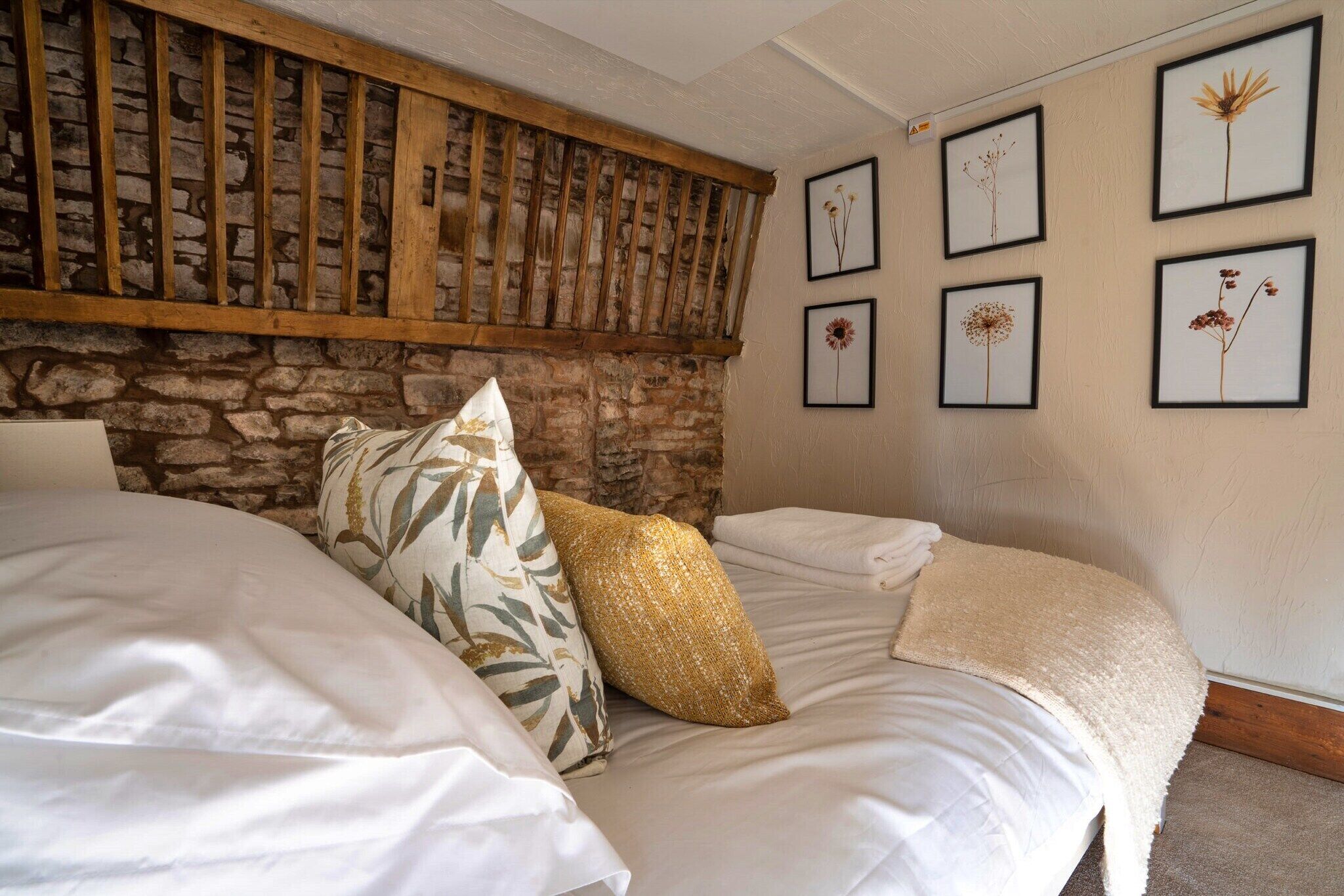 Ein Schlafzimmer mit Steinwand, Holzbalken und gerahmten Pflanzenbildern an der Wand.