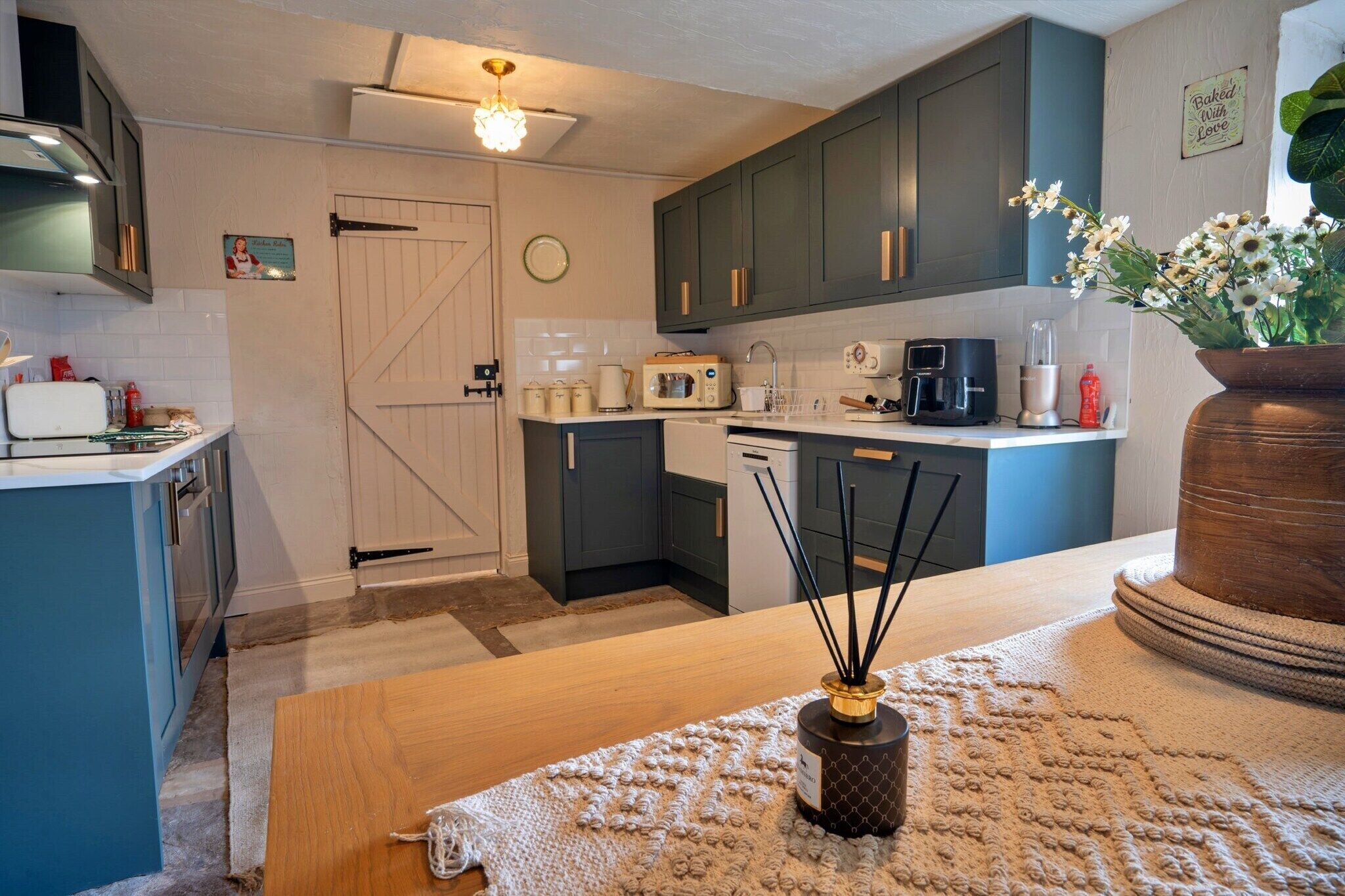 A modern kitchen with dark blue cabinets, a white door, and a wooden table with a decorative vase.