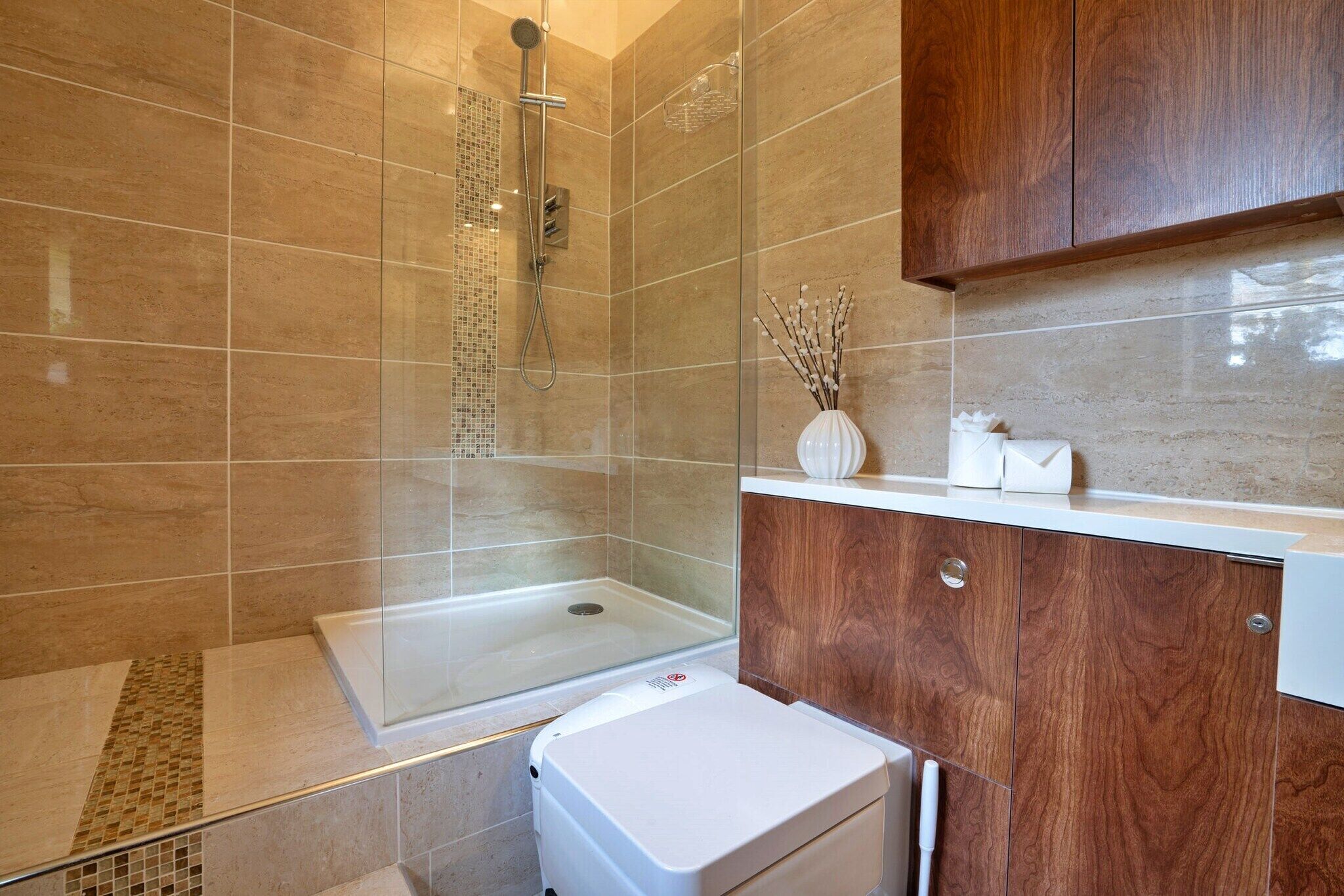 A modern bathroom with a glass-enclosed shower, a white toilet, and a wooden vanity with a mirror.