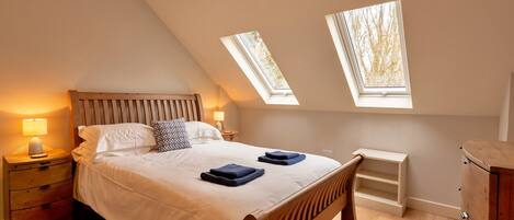 A bedroom with a sloped ceiling, two skylights, a wooden bed, a nightstand with a lamp, and a wooden dresser.