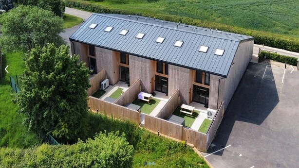 Un bâtiment moderne doté d’un toit en pente, de nombreuses fenêtres et d’une cour avec des espaces aménagés pour s’asseoir.
