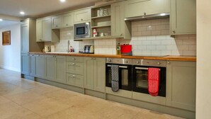 A modern kitchen with light green cabinets, a microwave, a toaster, and an oven. - Barn in Cotswolds with Private Hot Tub (Little Rissington)