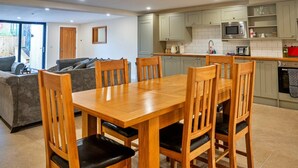 A modern kitchen with grey cabinets, a wooden dining table, and a grey sofa in the living area. - Barn in Cotswolds with Private Hot Tub (Little Rissington)