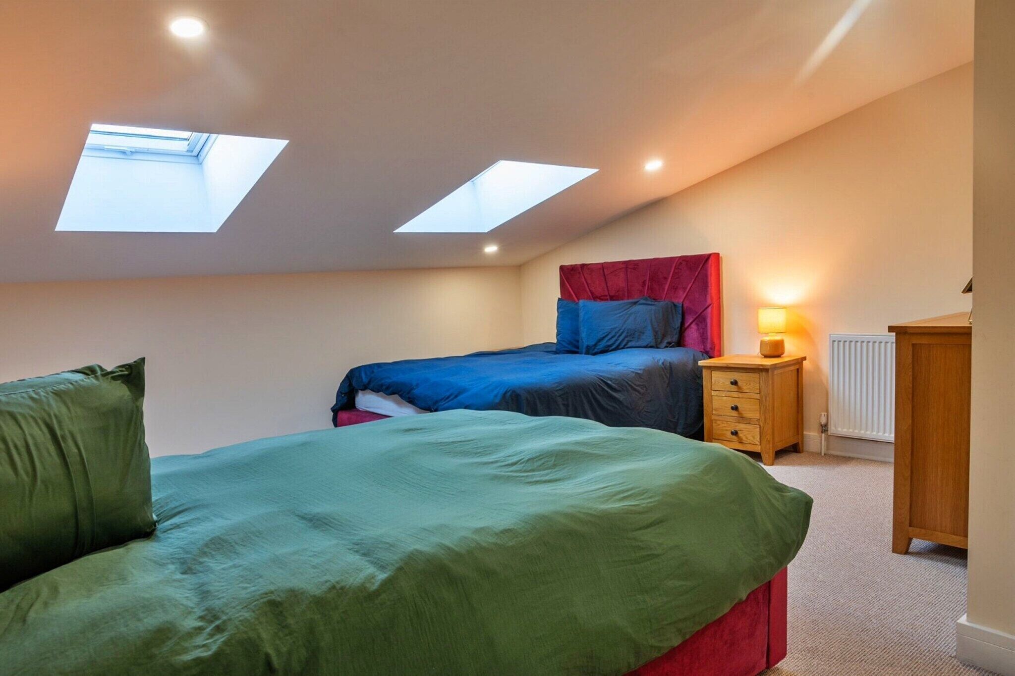 Quarto com duas camas, um claraboia, uma mesa de cabeceira e um radiador.