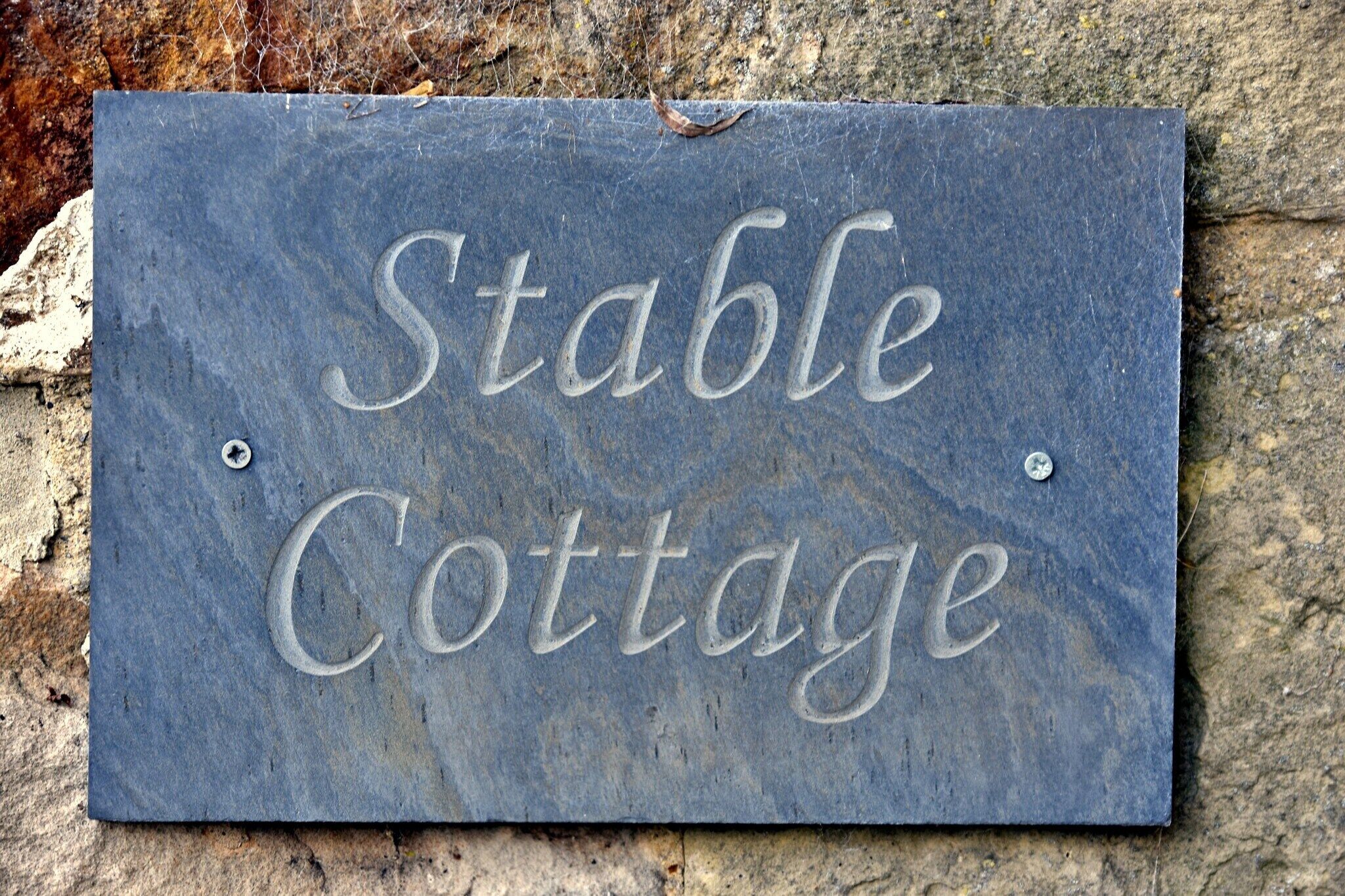 Ein aus Schiefer gefertigtes Schild mit der Aufschrift 'Stable Cottage', angebracht an einer Steinmauer.