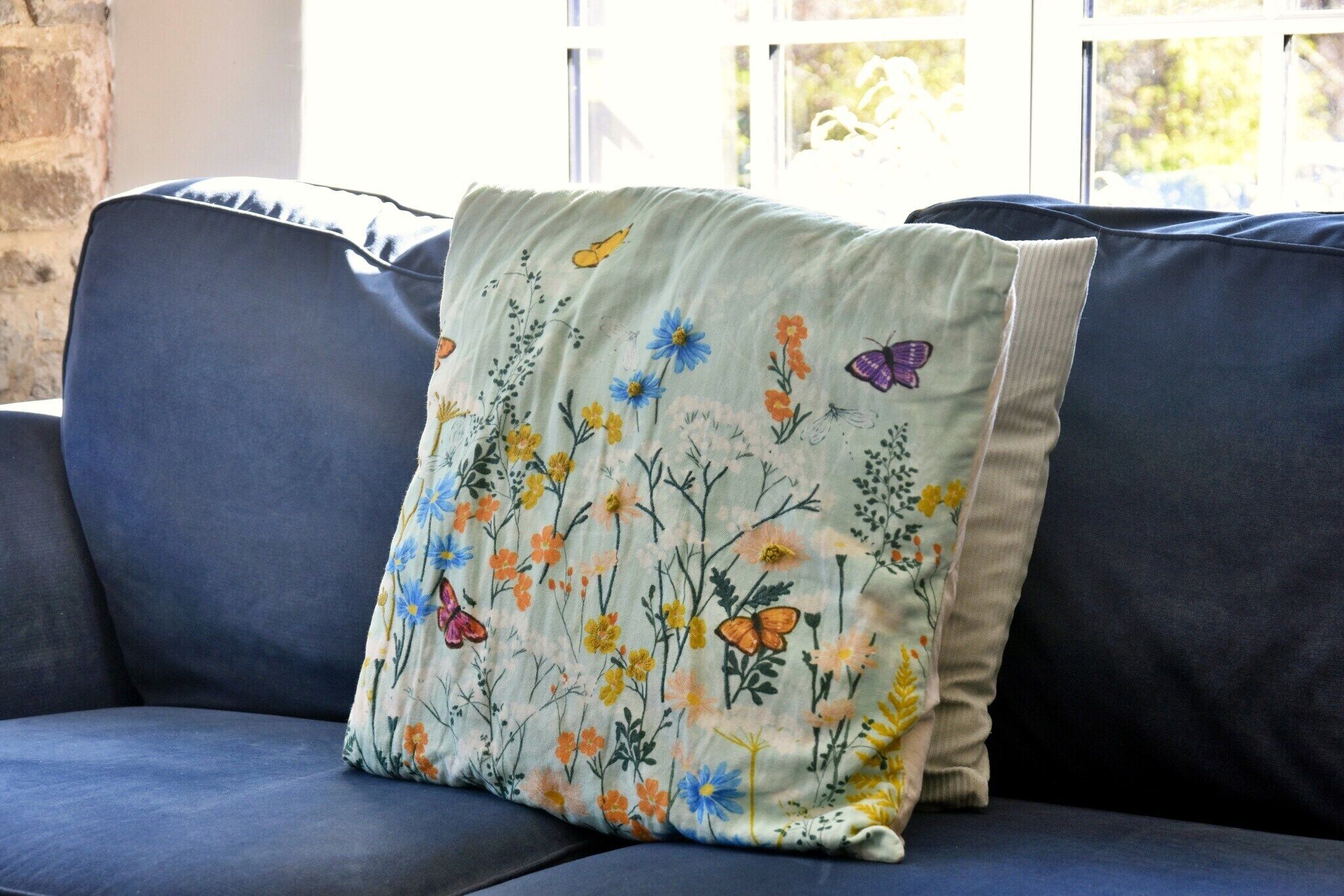 A dark blue sofa with a floral pillow featuring butterflies and flowers.