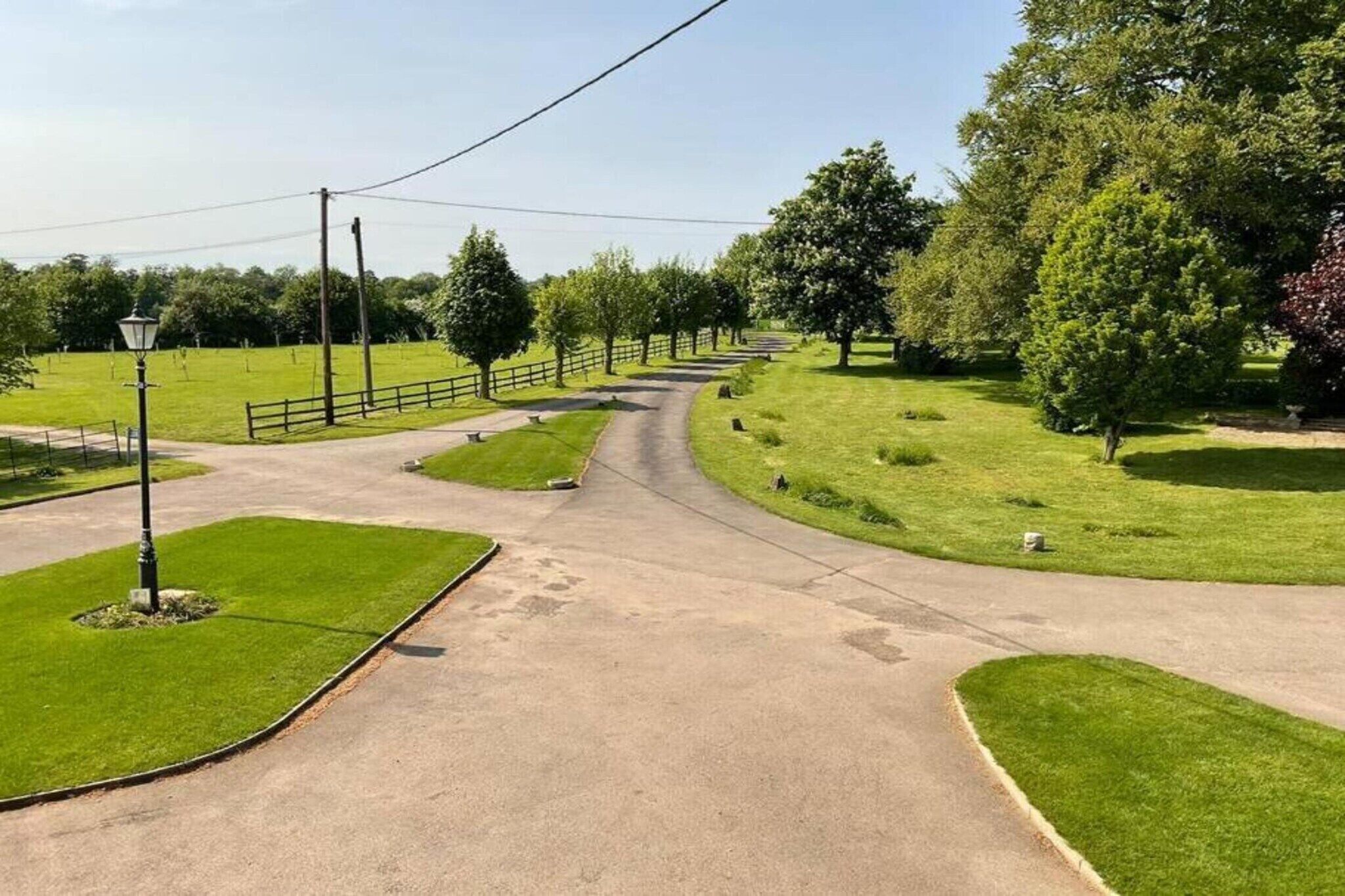 Een verhard kruispunt met een bochtige weg, omringd door groen gras en bomen.