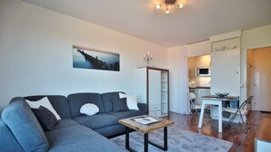 A modern living room with a grey sectional sofa, a wooden coffee table, and a dining area with a small kitchen.