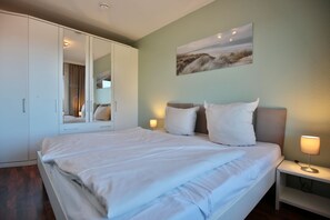 Quarto com uma cama grande, um guarda-roupa, uma mesa de cabeceira com abajur e um quadro na parede.