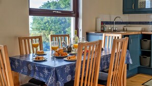 Uma mesa de jantar com toalha temática náutica, cadeiras de madeira e itens de café da manhã, como croissants e suco de laranja.